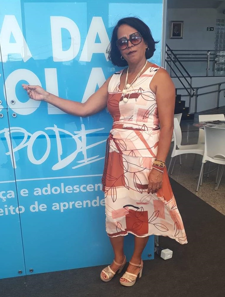 Gilva Cardoso, presidente do Conselho Municipal de Educação de Santo Estêvão (BA), está em pé em frente a um estande azul.