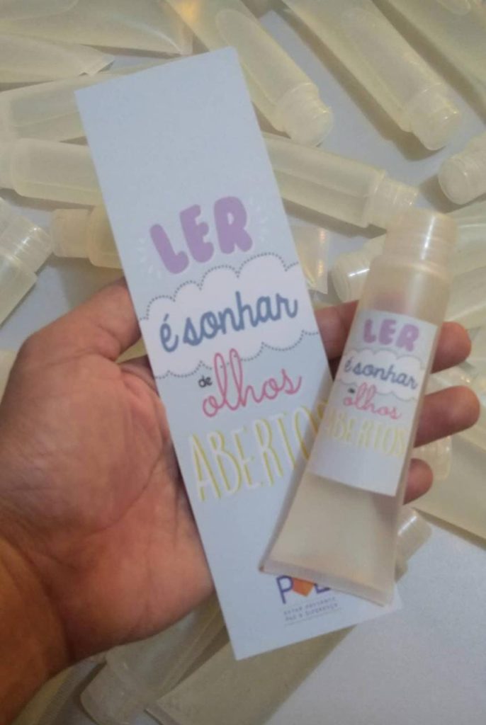 Imagem de marcador de livro e um frasco de álcool gel, entregues pelo projeto Delivery de livros na casa das pessoas.
