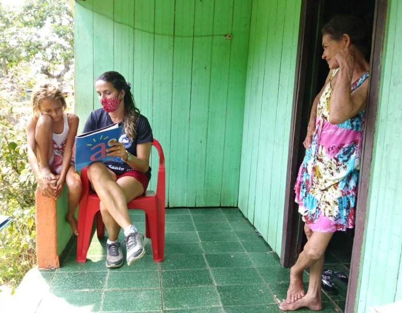 Imagem de uma cena de mediação de leitura, realizada por voluntários e voluntárias da ONG Vagalume na casa da família das crianças, em Cruzeiro do Sul (AC).